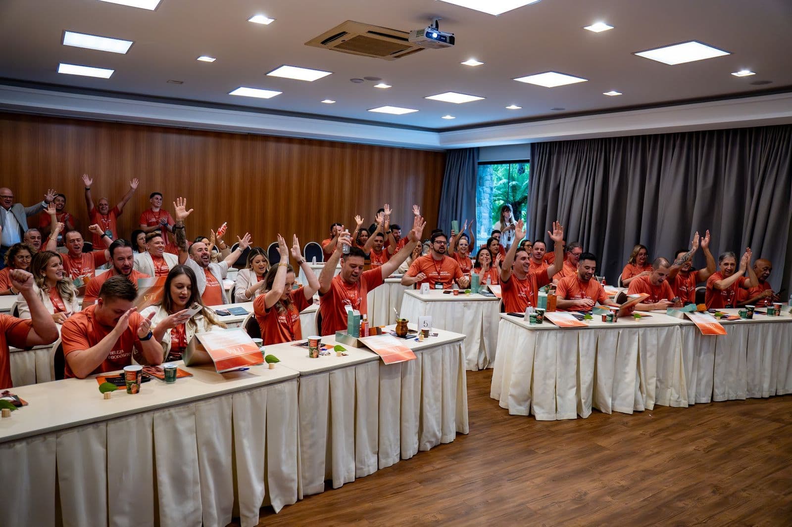 Sala cheia de distribuidores com camisetas da De Sírius comemorando na Convenção Conexão 2026